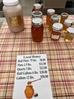 Jars of Ibach honey on a plaid tablecloth beside the Local Honey price sign